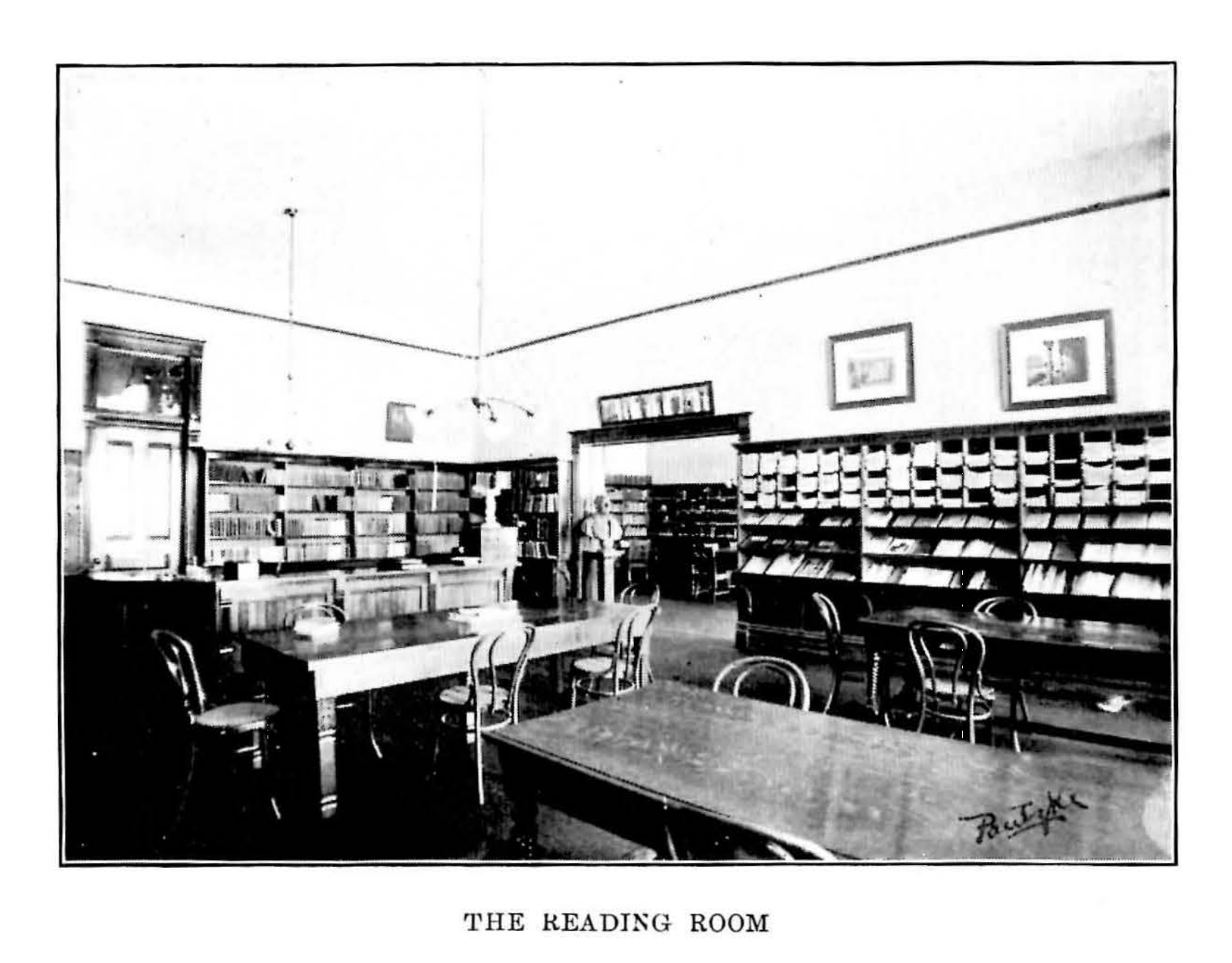 An image of a reading room in the library at CWU in 1903 from the 1903-04 CWU Catalogue. There are two large tables in the room and book shelves on several walls in the room.
